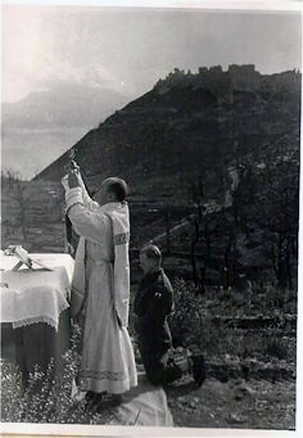 A Catholic Priest celebrating Mass being served by an Allied soldier; in the background the ruins of Monte Cassino Abbey.