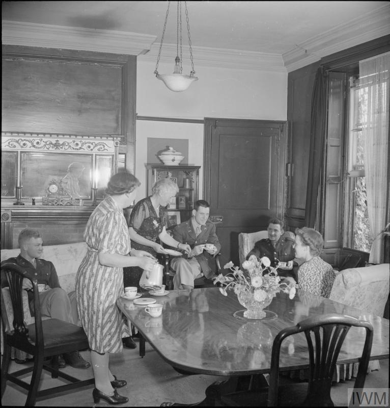 WINCHESTER, ENGLAND, ENTERTAINS US TROOPS: EVERYDAY LIFE WITH AMERICANS SOLDIERS IN WINCHESTER, HAMPSHIRE, ENGLAND, UK, 1944 (D 21565) Mrs A D Weller (left) pours tea for Lieutenant Loren Bacon (from Eugene, Oregon), Lieutenant Chas Raymond (from New York), Lieutenant J T Crane (from Chicago) during afternoon tea with friends at her home in Winchester, Hampshire. Copyright: © IWM. Original Source: http://www.iwm.org.uk/collections/item/object/205201158