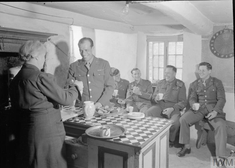 US TROOPS IN AN ENGLISH VILLAGE: EVERYDAY LIFE WITH THE AMERICANS IN BURTON BRADSTOCK, DORSET, ENGLAND, UK, 1944 (D 20156) British and American troops share a joke as they enjoy refreshments in the village canteen at Burton Bradstock, Dorset. The canteen is run by Mrs Howarth, the wife of the local schoolmaster, seen here pouring tea for Corporal Allan Decker (of 1657 S Central Park Avenue, Chicago). Corporal James Flower (of 173 High Plain Street, Walpole, Massachusetts) and Pfc Roy St Jean (of 292 Union Street, Spri... Copyright: © IWM. Original Source: http://www.iwm.org.uk/collections/item/object/205200866