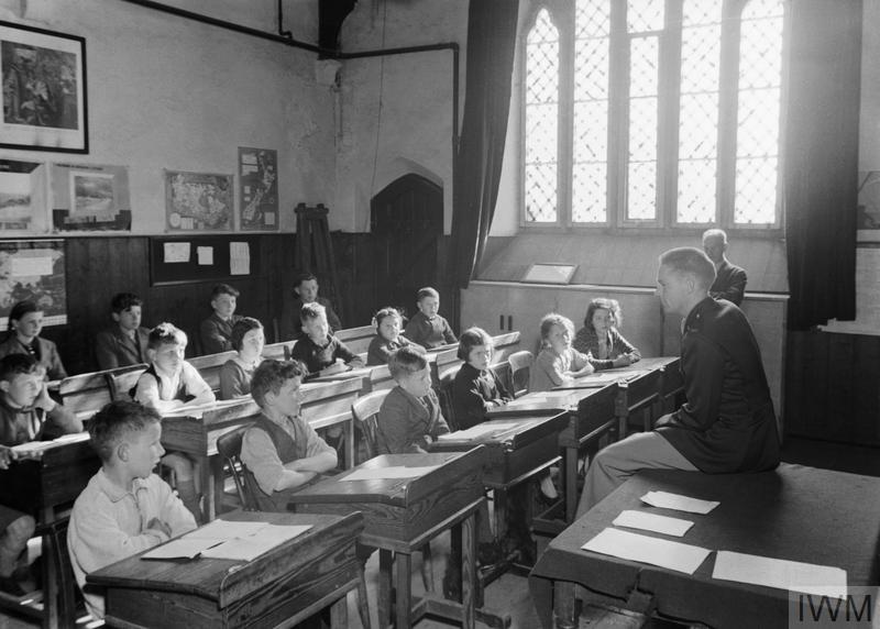 US TROOPS IN AN ENGLISH VILLAGE: EVERYDAY LIFE WITH THE AMERICANS IN BURTON BRADSTOCK, DORSET, ENGLAND, UK, 1944 (D 20140) In a classroom in the village school at Burton Bradstock, Dorset, American soldier Lieutenant Walker (of Box 617, Adar Grove Station, Shreveport, Louisiana) gives a talk to a group of children about life in the United States.  According to the original caption, Lt Walker's brother is Principal of a school, and before the war Lt Walker worked for the Southern Bell Telephone Company. Copyright: © IWM. Original Source: http://www.iwm.org.uk/collections/item/object/205200859
